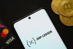 A smartphone displaying the 'XRP LEDGER' logo resting next to gold Bitcoin coins and a Visa card.