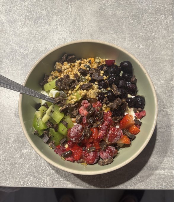 A vibrant breakfast bowl filled with kiwi, strawberries, raspberries, blueberries, granola, and cacao nibs, likely yogurt-based, sitting on a gray surface. The colorful, nutrient-packed meal visually complements the optimistic "first win" reference in the post, offering a bright contrast to the week's rough market performance.