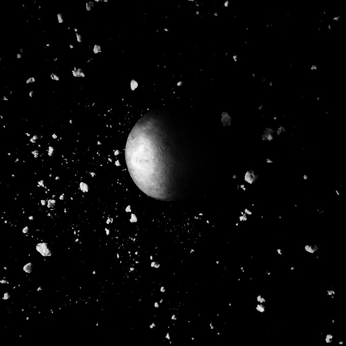 A grayscale image showing a spherical celestial body, possibly a planet or moon, surrounded by scattered asteroids or debris against a black space background.