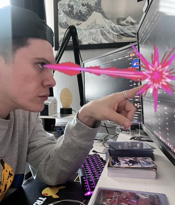 A person wearing a cap and gray sweatshirt sitting at a desk with multiple monitors and a pink-lit keyboard, with pink and red laser-like visual effects added over the image.