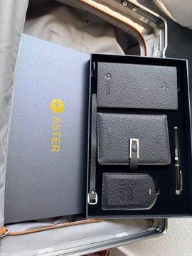 A luxury Aster gift set featuring three black leather goods with silver hardware and a branded pen is displayed in its presentation box. The post expresses gratitude for receiving this premium set as an outfit addition from Aster DEX.