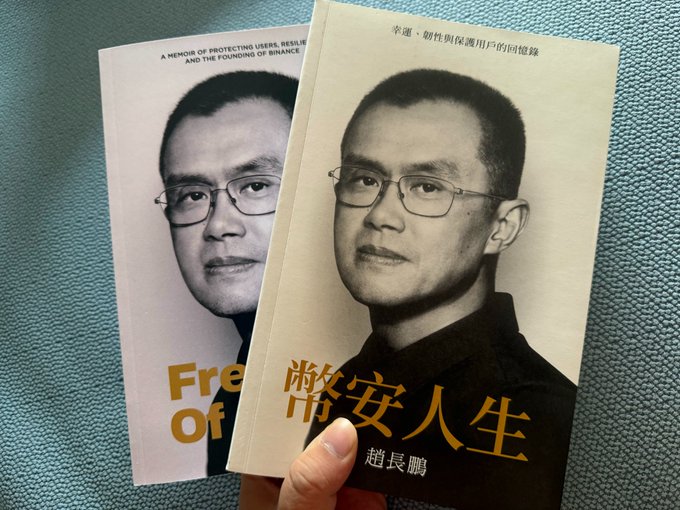 A hand holds two copies of CZ's memoir "Free of..." (English) and "幣安人生" (Chinese), both featuring a portrait of Changpeng Zhao in glasses, with a noticeable color tone difference between the cream-colored Chinese version and the white English version that the user humorously questions as a possible sign of a pirated copy.