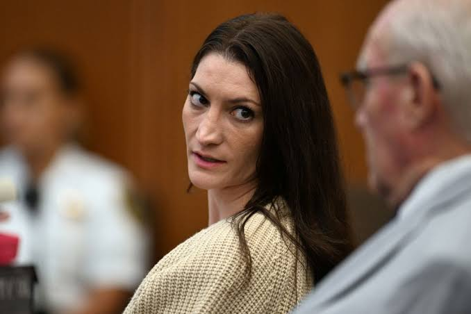 A courtroom scene featuring a woman with dark hair looking over her shoulder, with a blurred figure in uniform and another person partially visible in the foreground.
