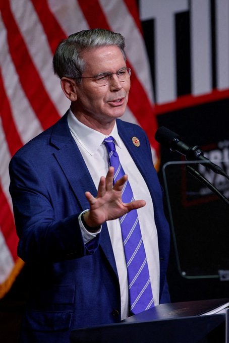 U.S. Treasury Secretary Scott Bessent speaks at a podium with an American flag behind him, emphasizing the importance of the Clarity Act for America to win the global race and highlighting the role of bank regulation.