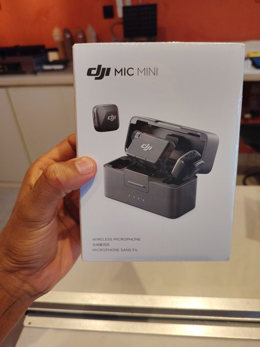 A hand holding the retail box for a DJI Mic Mini wireless microphone, showing the product image on the packaging.