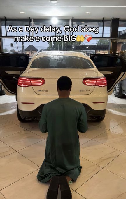 A man in a green robe kneels on a tiled floor in front of a white Mercedes-Benz GLC 43 with open doors. Text overlay reads: 'As e Dey delay, God abeg make e come BIG 🙌❤️'.