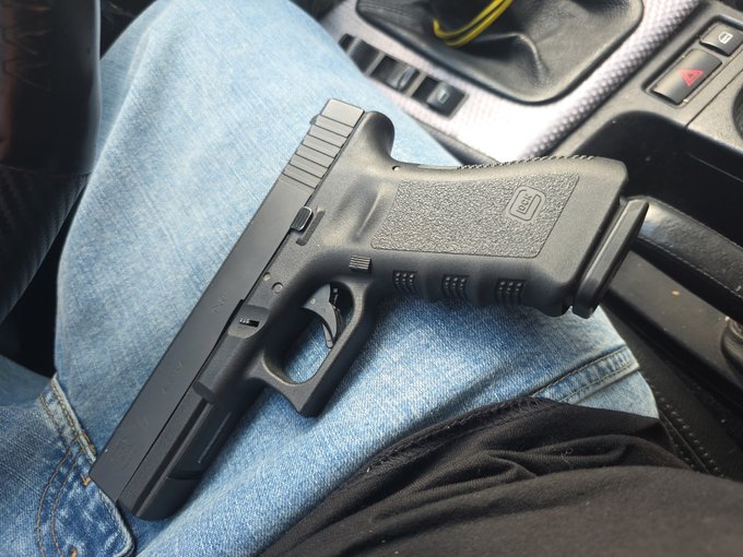 iced tea is poured into a black plastic cup, with the handle of the gun resting on the armrest of a car seat.