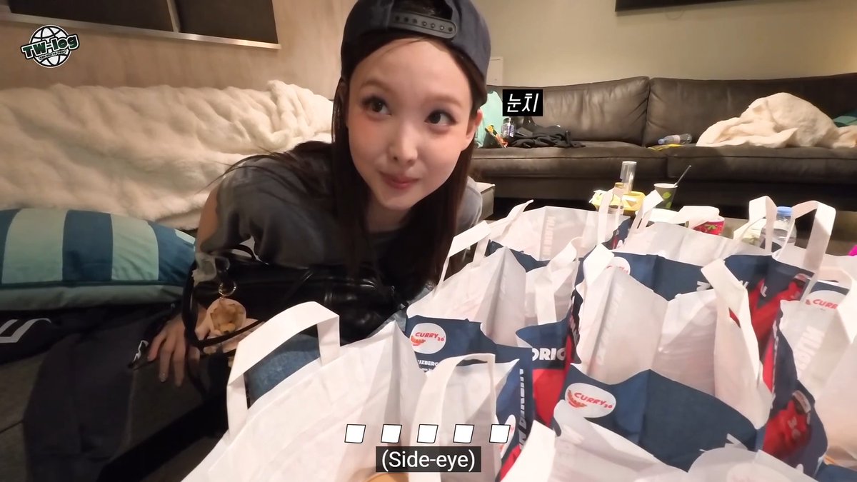A woman wearing a backwards cap smiles while giving a side-eye glance toward the camera, surrounded by multiple 'Curry' shopping bags in a living room setting, with a '(Side-eye)' caption below.