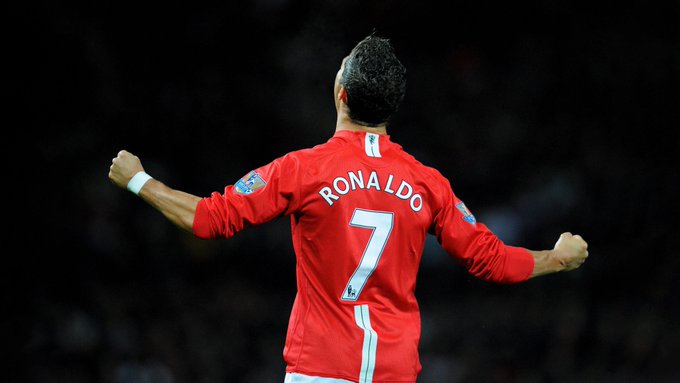 A rear-view photograph of soccer player Cristiano Ronaldo wearing a red Manchester United jersey with 'RONALDO' and the number 7, celebrating with raised fists at night during a match.