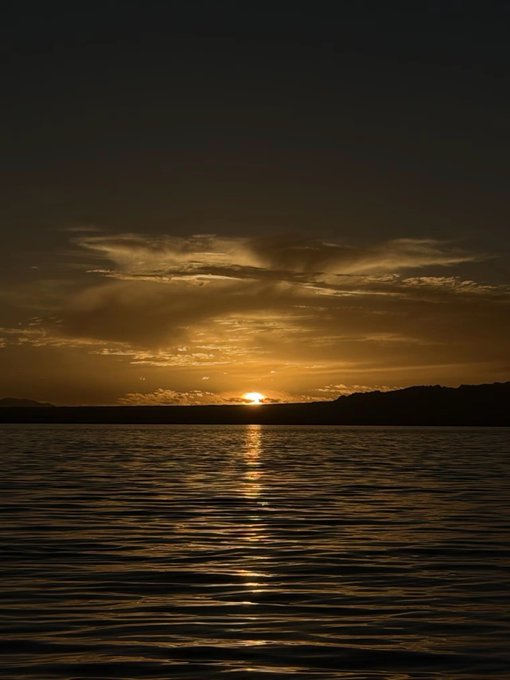A serene sunset over a calm body of water, with the sun casting a golden reflection across the dark waves.