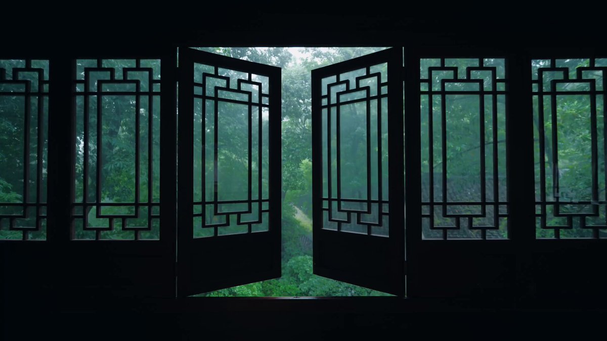The image features a black door with an open design, allowing light to enter from behind. The door is located within a room that has a window with a lattice pattern. The scene takes place during the day under cloudy skies, creating a moody atmosphere. The combination of the dark door and the cloudy sky adds depth and contrast to the image.