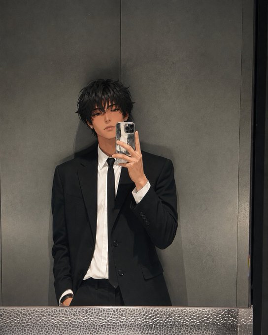 A young man with dark hair wearing a black suit, white shirt, and black tie takes a mirror selfie with his phone in a gray-walled bathroom.