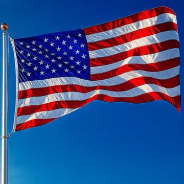 An American flag waves against a clear, bright blue sky, attached to a flagpole on the left side of the frame.