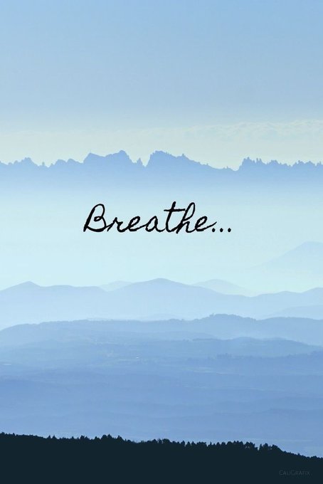 A serene layered landscape of blue-toned mountains under a hazy sky with the word 'Breathe...' written in cursive text across the center.