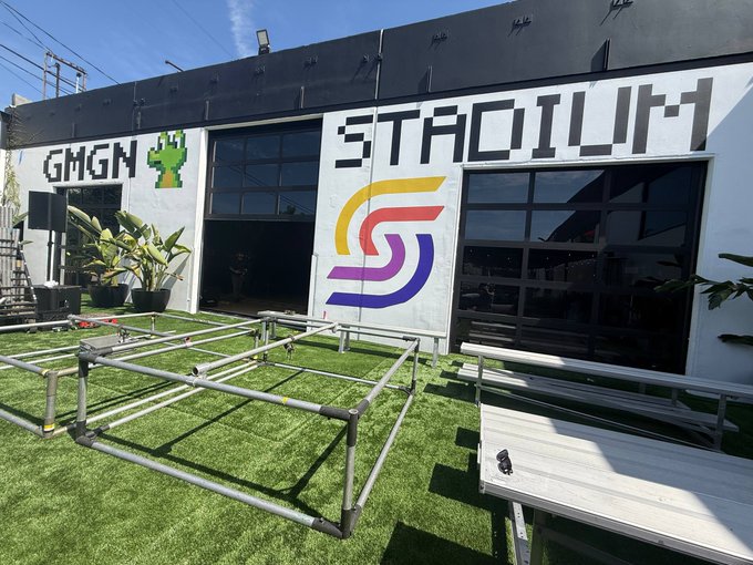An outdoor patio area with artificial grass and picnic tables sits in front of a building with 'GMGN' and a cactus logo on the left, and 'STADIUM' above a stylized 'S' logo on the right.