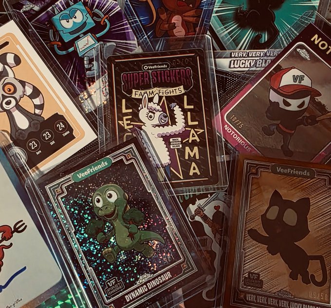 Collection of Veefriends trading cards including 'SUPERSTICKERS FAME FIGHTS LLAMA', 'DIAMOND DINOSAUR', and other character cards scattered together.