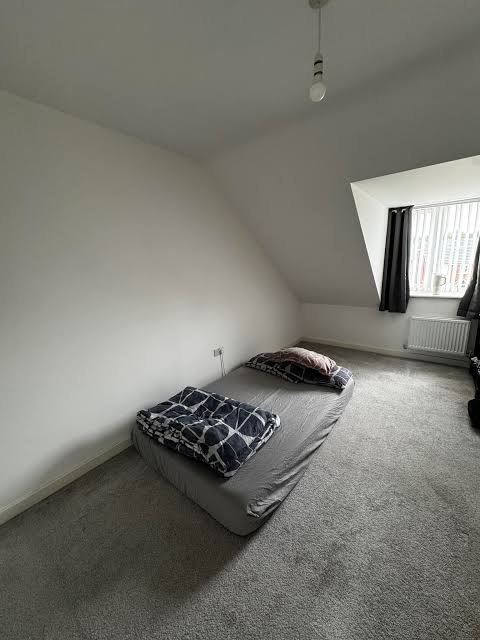 A minimalist bedroom with a gray bed, patterned pillows, and a sloped ceiling is shown, where natural light from the window creates a calm space to focus on financial matters like checking on $ANSEM's price movement.