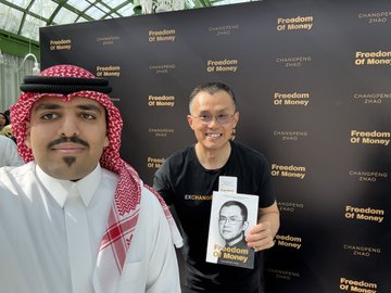 Two men pose in front of a "Freedom of Money" and "Changpeng Zhao" backdrop, with one man wearing traditional Saudi attire and the other in a black t-shirt holding a copy of "Freedom of Money" featuring CZ's face, tying into the post's playful comparison between CZ (Binance) and blknoiz06 as crypto personalities.
