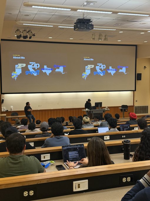 A lecture hall scene shows a presenter standing at the front near a large screen displaying 'About Me' with tech company logos including Purdue (P), Zip, Intuit, Coinbase, Google, and Capital One, while students sit at desks with laptops.