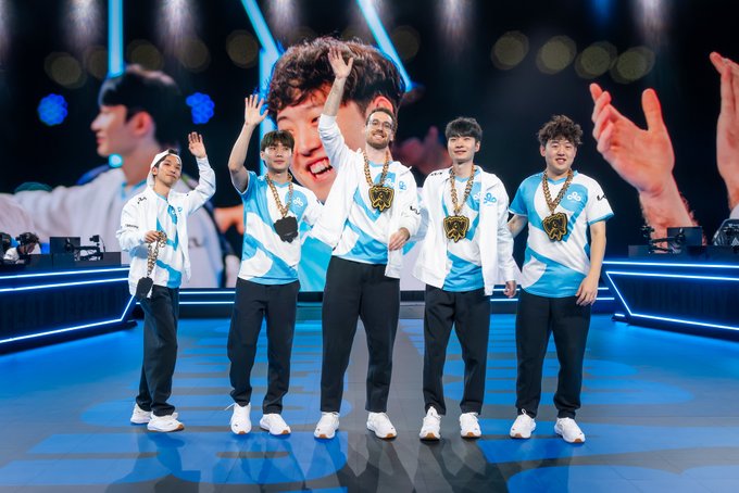 Five members of an esports team wearing blue and white Cloud9 jerseys and championship medals, celebrating on a stage with a large screen behind them.