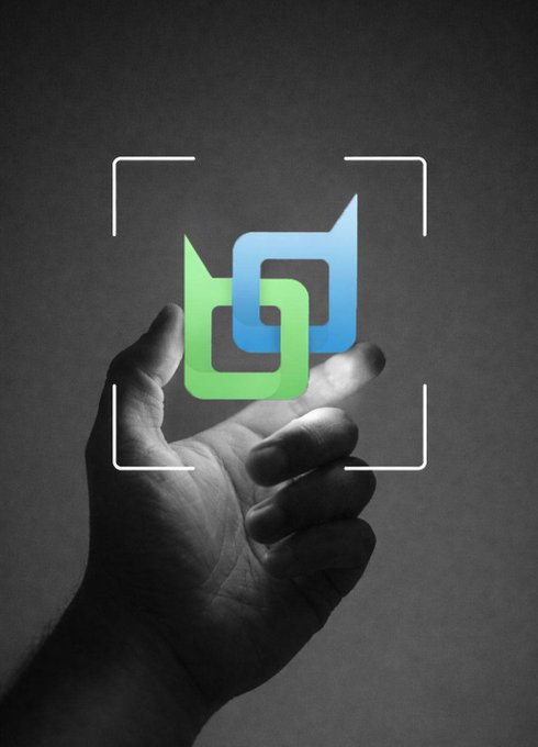 A hand reaching up to hold an illuminated green and blue interlocking logo within a white camera viewfinder frame against a dark background.