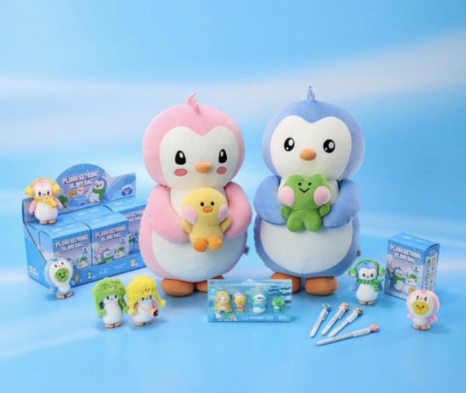 Two plush penguin characters, one pink holding a yellow chick and one blue holding a green dinosaur, stand on a blue background surrounded by 'Planet Beyond' blind box figures and merchandise.