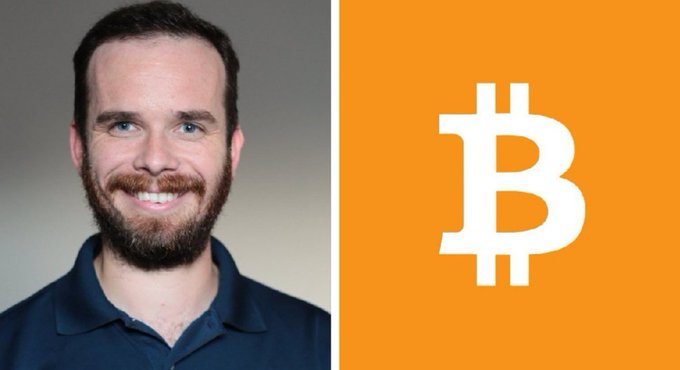 A smiling bearded man in a navy polo shirt appears beside the iconic white Bitcoin logo on an orange background, visually representing Pierre Rochard, the Bitcoin advocate referenced in the post about BTC's potential undervaluation given its 21 million supply cap and growing institutional adoption.