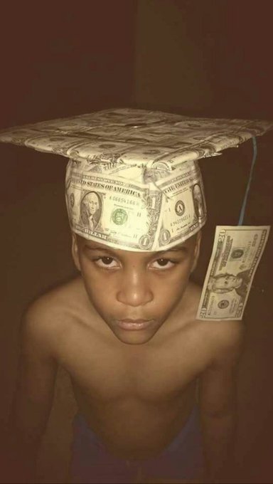 A young person wearing a graduation cap made from a US dollar bill, with a one-hundred dollar bill tassel, looking directly at the camera.