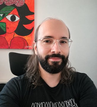 The image features a man wearing glasses, sitting down, and smiling at the camera. He has long hair and is dressed in a black shirt. Behind him, there is an abstract painting of a woman with red eyes and green face on the wall. The text "be @mert for Solana for years, make generational wealth in tokens in that time randomly for no reason whatsoever decide to push tranny privacy coin" can be seen, which seems unrelated to the main subject of the image - the man sitting down and smiling at the camera.