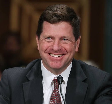 A smiling man in a dark suit and red patterned tie speaks into a microphone in what appears to be a formal government hearing setting. The image relates to the post about Jay Clayton, the former SEC Chair who became known for his stance against XRP, now being appointed as White House AI czar under President Trump.