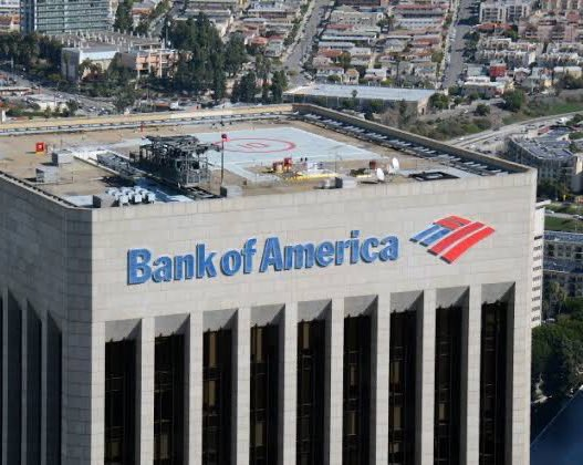 An aerial view of a Bank of America building with its logo prominently displayed, set against a city backdrop, illustrating the context of the bank's CEO discussing the U.S. banking industry's potential adoption of cryptocurrency for payments.
