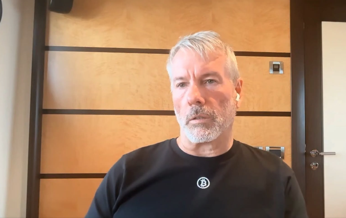 A gray-haired bearded man in a black t-shirt with a small circular logo sits in front of a wooden paneled wall, likely discussing his investment experience with MicroStrategy (MSTR) and his advice to consider STRC as an alternative.
