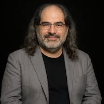 urn of water, a man with long hair and glasses, dressed in a gray suit jacket against a black background.