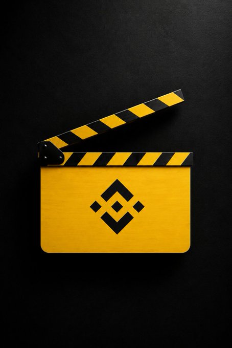 A yellow clapperboard with black and yellow hazard stripes on the open clapper arm features the Binance logo (a geometric diamond design), symbolizing the start of a new chapter—fitting the "GM" and "on your marks" message about a fresh beginning.