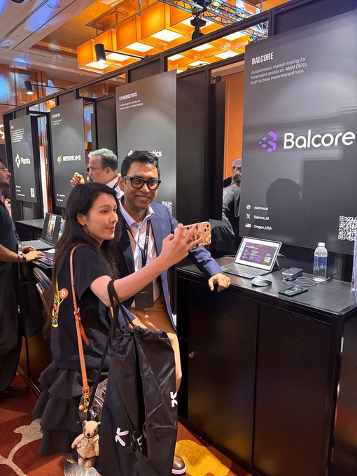 Two people pose for a selfie at a crypto/blockchain conference booth labeled 'Balcore' with the tagline 'Autonomous market making for AMM DEX built to beat impermanent loss.'