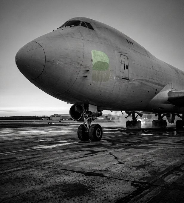 A large commercial cargo aircraft (appears to be a Boeing 747) sits on the tarmac in a moody, desaturated black-and-white photo, with only a small green logo patch on its fuselage providing a pop of color. The image's symbolism of a heavy jet needing substantial runway to achieve liftoff mirrors the post's message about Boba's clear, non-complicated path to success—so long as runway, progress, and strategy are in place, the binary answer is simply "yes."