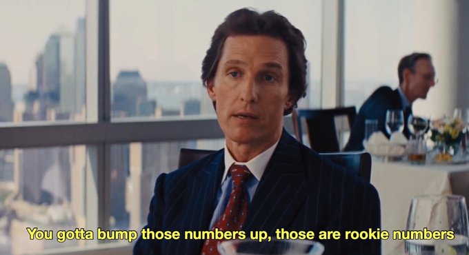 A scene from a film featuring a man in a pinstripe suit with the caption "You gotta bump those numbers up, those are rookie numbers" displayed at the bottom.