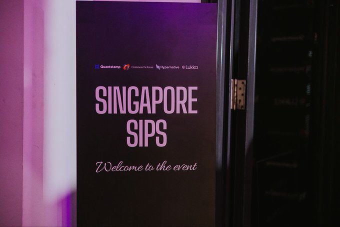 A dark purple welcome sign for an event reading 'SINGAPORE SIPS Welcome to the event', featuring logos for Quantstamp, Coinbase Developer, Hypernative, and Lukka at the top.