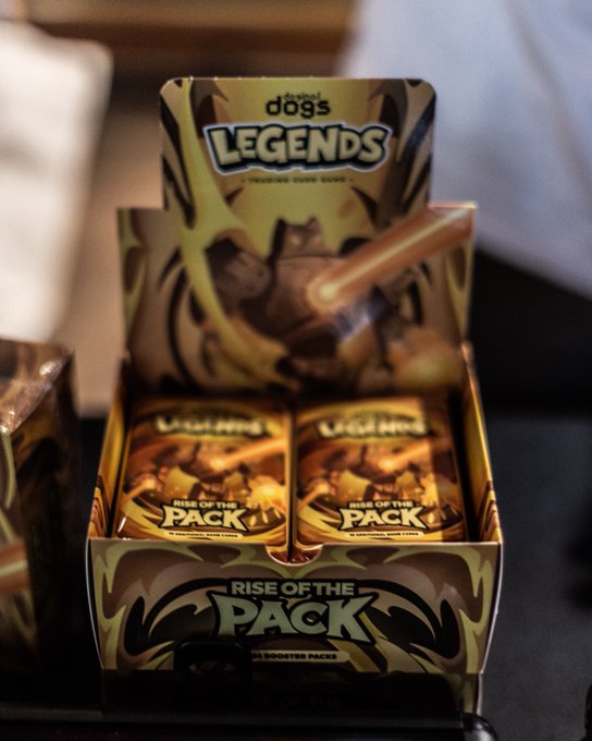 A display box of 'Top Dog's LEGENDS Rise of the Pack' trading card game booster packs, featuring gold and black artwork with a character design on the packaging.