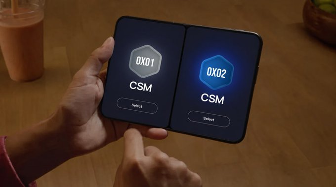 A pair of hands holds a foldable dual-screen device displaying a menu with two options labeled '0X01 CSM' and '0X02 CSM' (highlighted in blue), each with a 'Select' button, against a wooden table background with an iced drink visible.