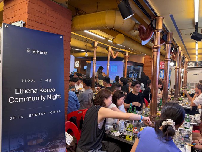 A banner reading 'Ethena Korea Community Night SEOUL / 서울 GRILL · SOMAEK · CHILL' stands in a bustling, dimly lit restaurant with copper exhaust pipes hanging from the ceiling.
