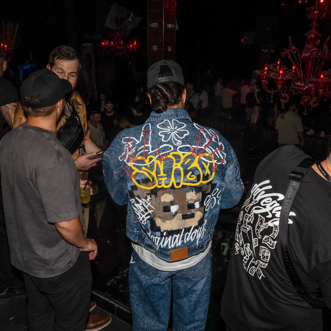 Back view of a person at a nightclub wearing a heavily customized denim jacket featuring graffiti-style 'SIR Royal' lettering, a pixel-art character, and 'original don' embroidery.