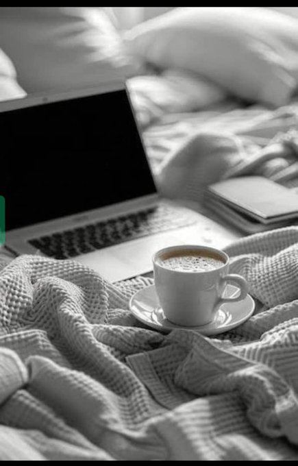 The image features a laptop computer sitting on top of a bed with a white cup of coffee placed next to it. The scene appears to be set in black and white, which adds a timeless quality to the composition. The focus of the image is on the laptop and its surroundings, creating an atmosphere that evokes a sense of relaxation or contemplation.