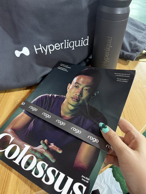 A hand holds a Colossus magazine featuring Devin Haney as the Issue 06 cover, in front of a Hyperliquid tote bag and matching black thermos bottle.