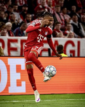 A Bayern Munich soccer player in a red jersey and shorts jumps to control the ball with his chest during a match.