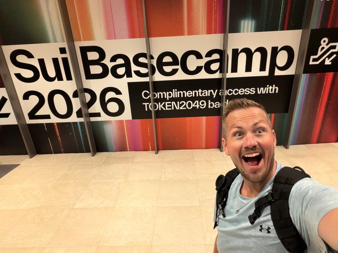A selfie of an excited man in front of a sign that reads 'Sui Basecamp 2026' with 'Complimentary access with TOKEN2049 badge' below.