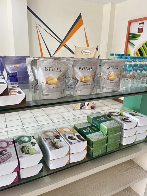 The image shows a display of packaged snacks including "BITLIZ ROTI BAGELEN" bags, bottled water, and stacked boxes of Amanda Brownies on glass shelves. The giveaway caption invites people to choose an Amanda Brownies variant or $5 prize, with the display showcasing the treats being offered.