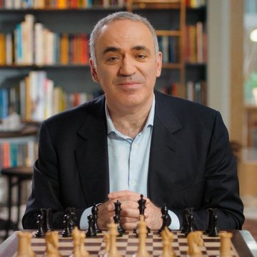 A confident, middle-aged man in a dark blazer smiles behind a chessboard set up with pieces. The image visually mirrors the quote's themes of strategy and finite versus unlimited control, framing the speaker as a grandmaster contrasting Bitcoin's 21 million supply cap against the Federal Reserve's open-ended money creation.