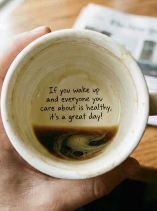 A hand holds a coffee mug (viewed from above) with the remaining drops of coffee inside, featuring the printed message: "If you wake up and everyone you care about is healthy, it's a great day!" — a simple, grounding reminder that connects to the post's sentiment about prioritizing health and loved ones over the fast-paced nature of crypto trading.