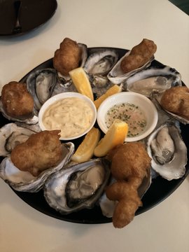 A platter of fried oysters on the half shell arranged around two dipping sauces (one tartar, one mignonette) with lemon wedges, representing a celebratory night out — likely funded by investment profits — after weeks of staying home.